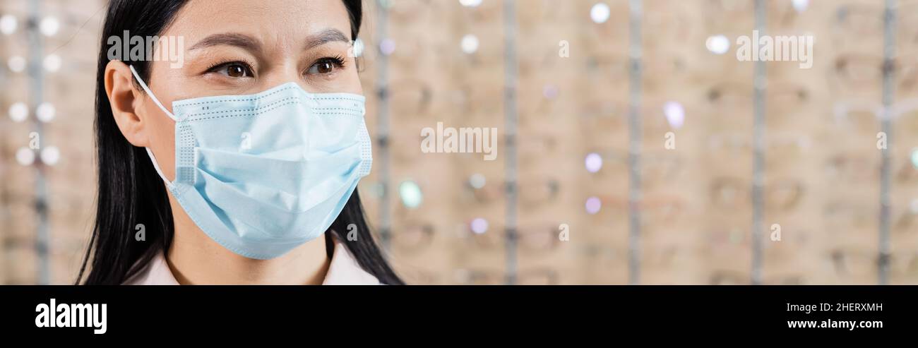 oftalmologo asiatico in maschera medica in salone di ottica su sfondo sfocato, banner Foto Stock