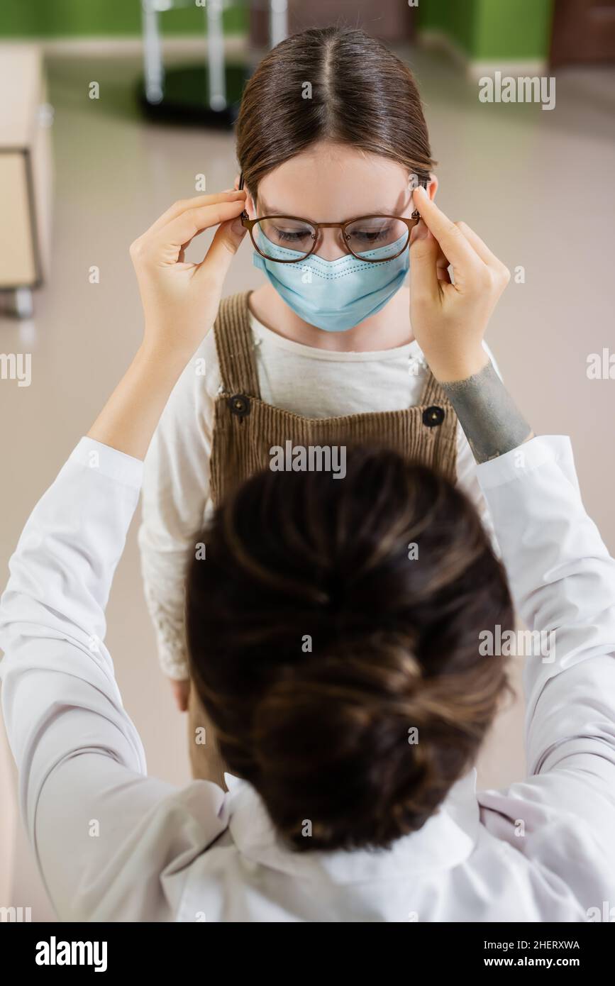 oftalmologo blurred che prova gli occhiali sul bambino nella maschera medica nel deposito dell'ottica Foto Stock