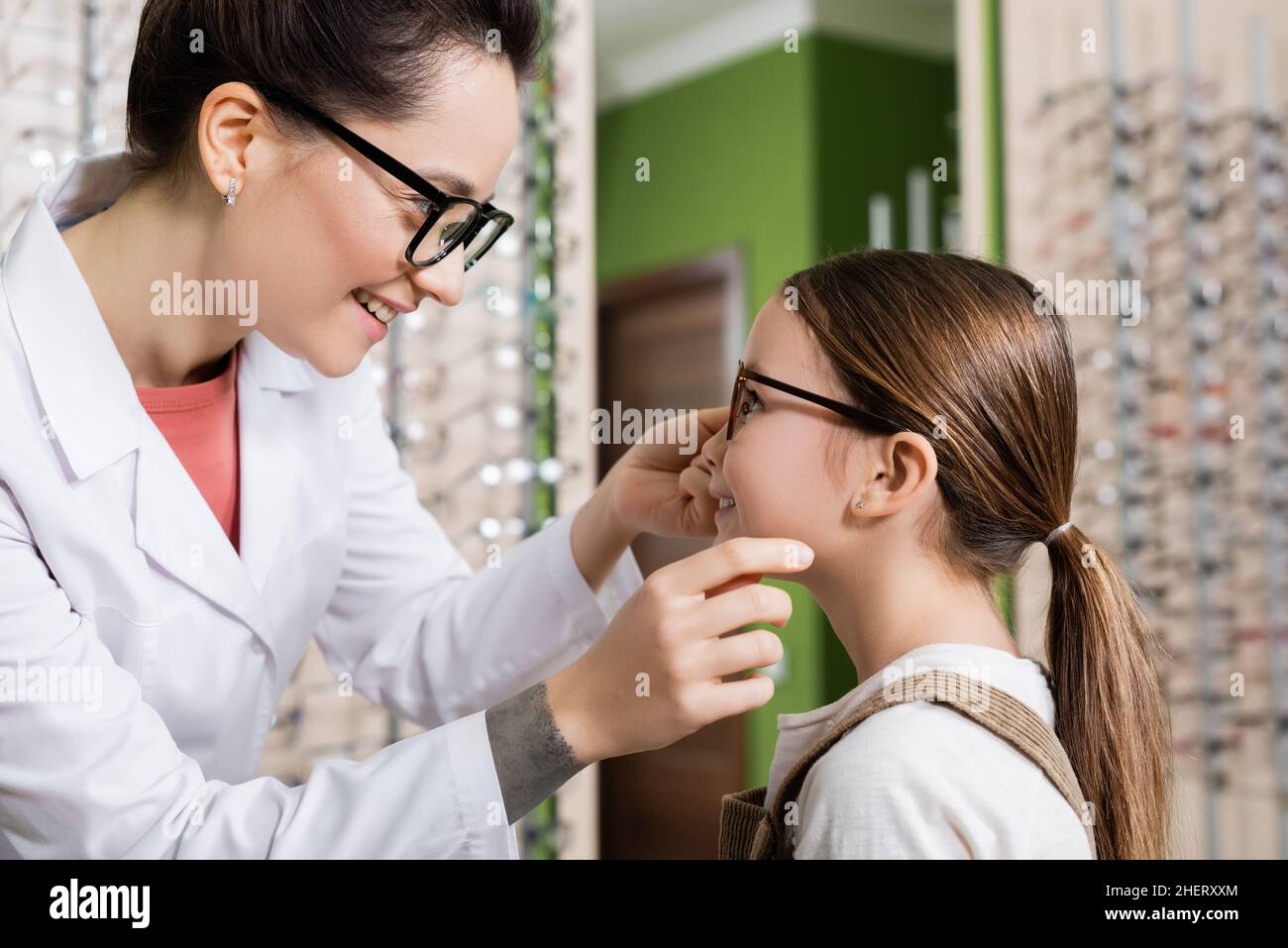 vista laterale dell'oftalmologo sorridente che prova gli occhiali sul bambino in salone dell'ottica Foto Stock