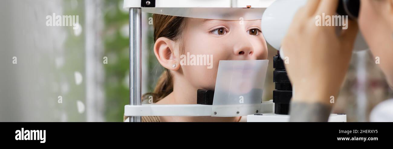 oculista blurred che controlla la vista della ragazza sul visore di visione in negozio di ottica, banner Foto Stock