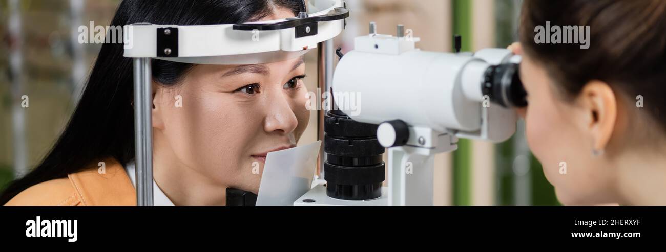 oftalmologo offuscato che misura la vista della donna asiatica su vision screener, banner Foto Stock