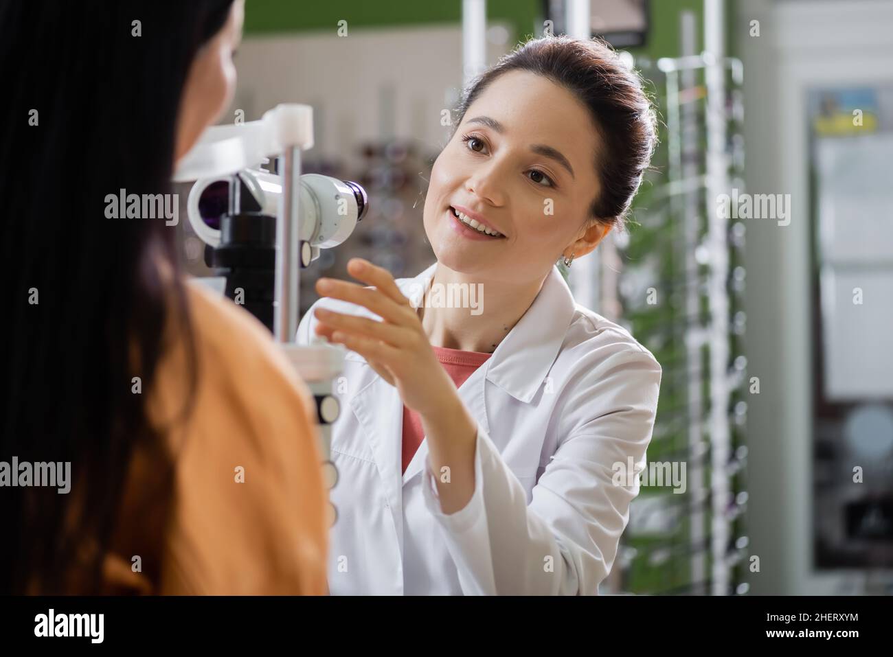 oftalmologo positivo che punta con la mano vicino alla donna sfocata e screener di visione Foto Stock