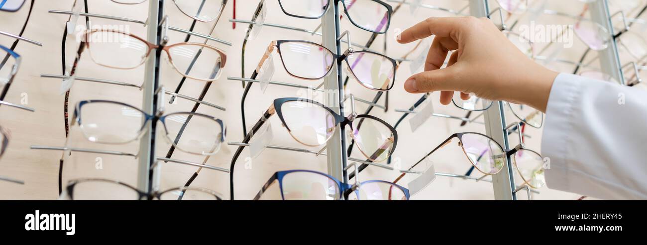 vista ritagliata di oculista prendendo occhiali in negozio di ottica, banner Foto Stock