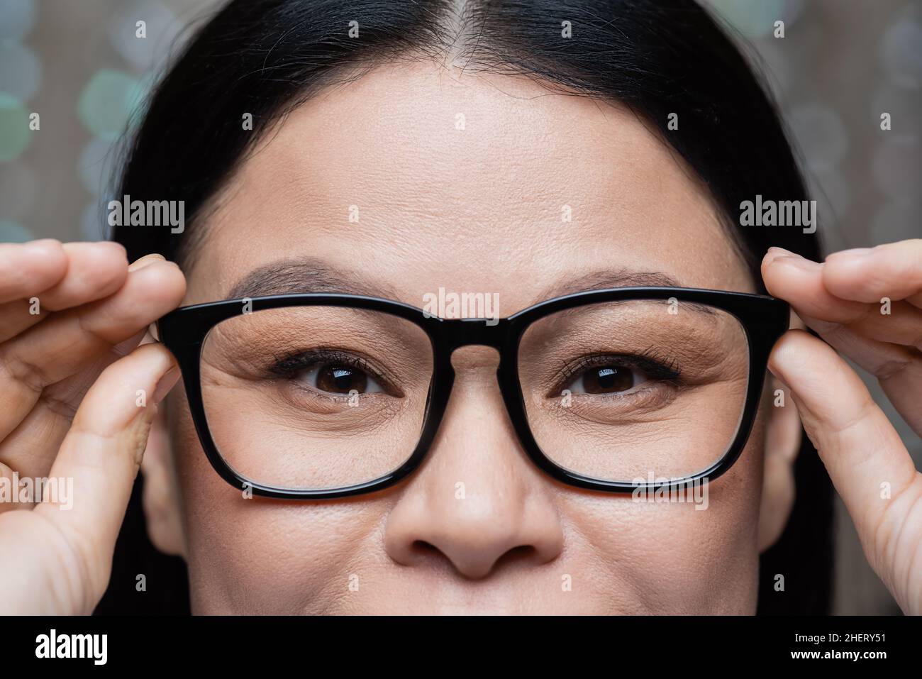 vista ritagliata della donna asiatica che tocca gli occhiali e guarda la macchina fotografica, concetto di cura degli occhi Foto Stock