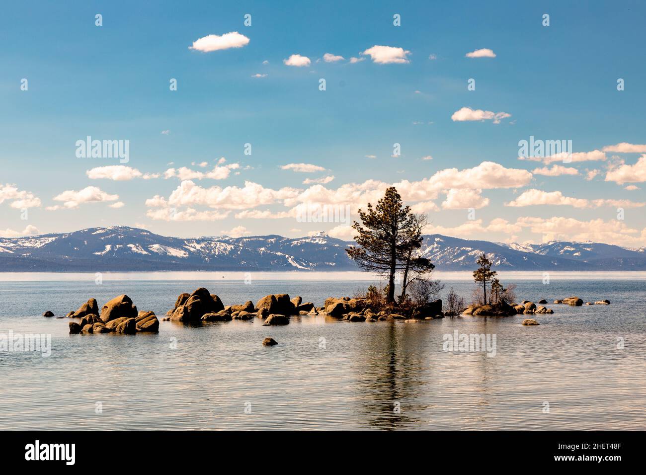 Una piccola isola con un albero nel lago Tahoe con le nuvole e montagne innevate nella catena montuosa della Sierra in California e Nevada USA Foto Stock