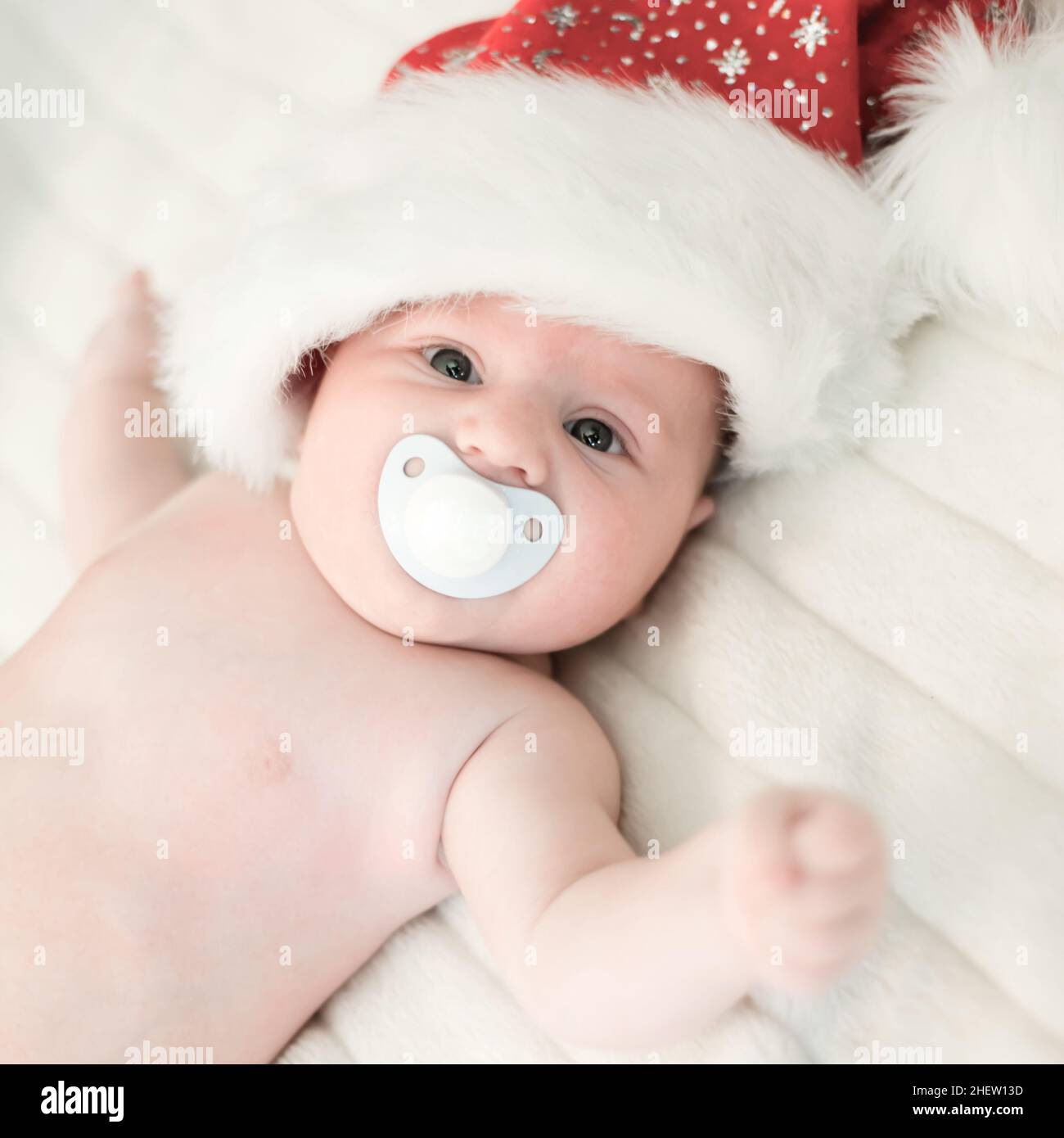 bimbo natalizio con cappuccio babbo natale e succhietto sdraiato su coperta bianca Foto Stock