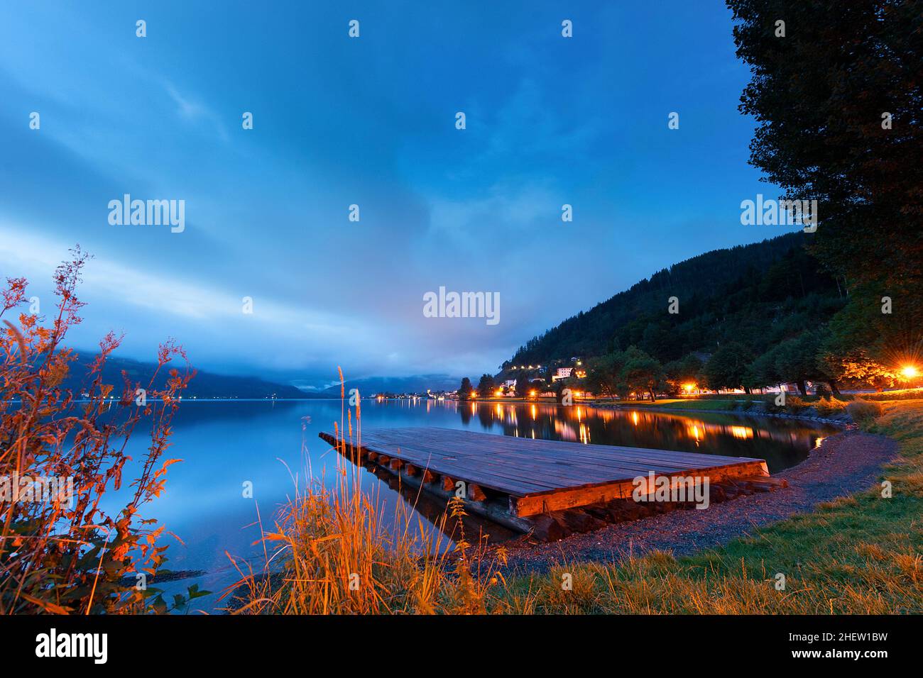 Tramonto su un lago tranquillo con un molo di legno e luci colorate che costeggiano la riva Foto Stock