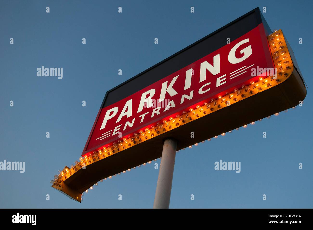 grande cartello rosso illuminato con molte lampade e freccia arancione sul palo con cielo blu Foto Stock