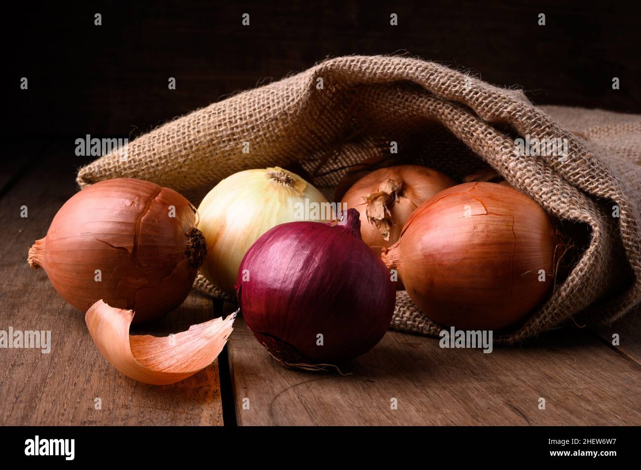 Cipolle rosse e bianche su un rustico tavolo di legno che fuoriesce da un sacco di stoffa in cucina, vista dall'alto. Foto di alta qualità Foto Stock