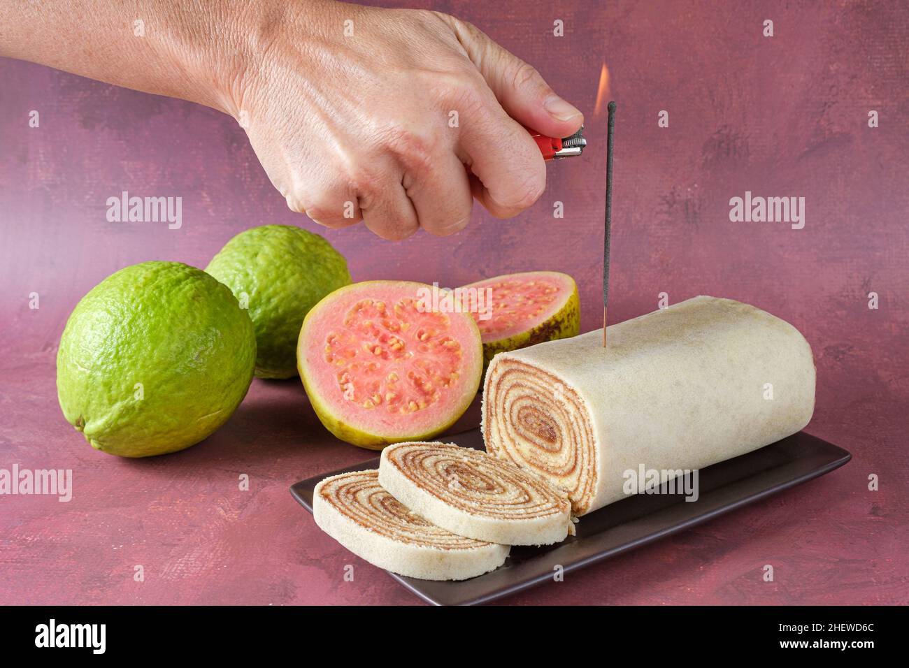 Donna che illumina una candela scintilla su un rotolo di torta accanto alle guavas. Foto Stock