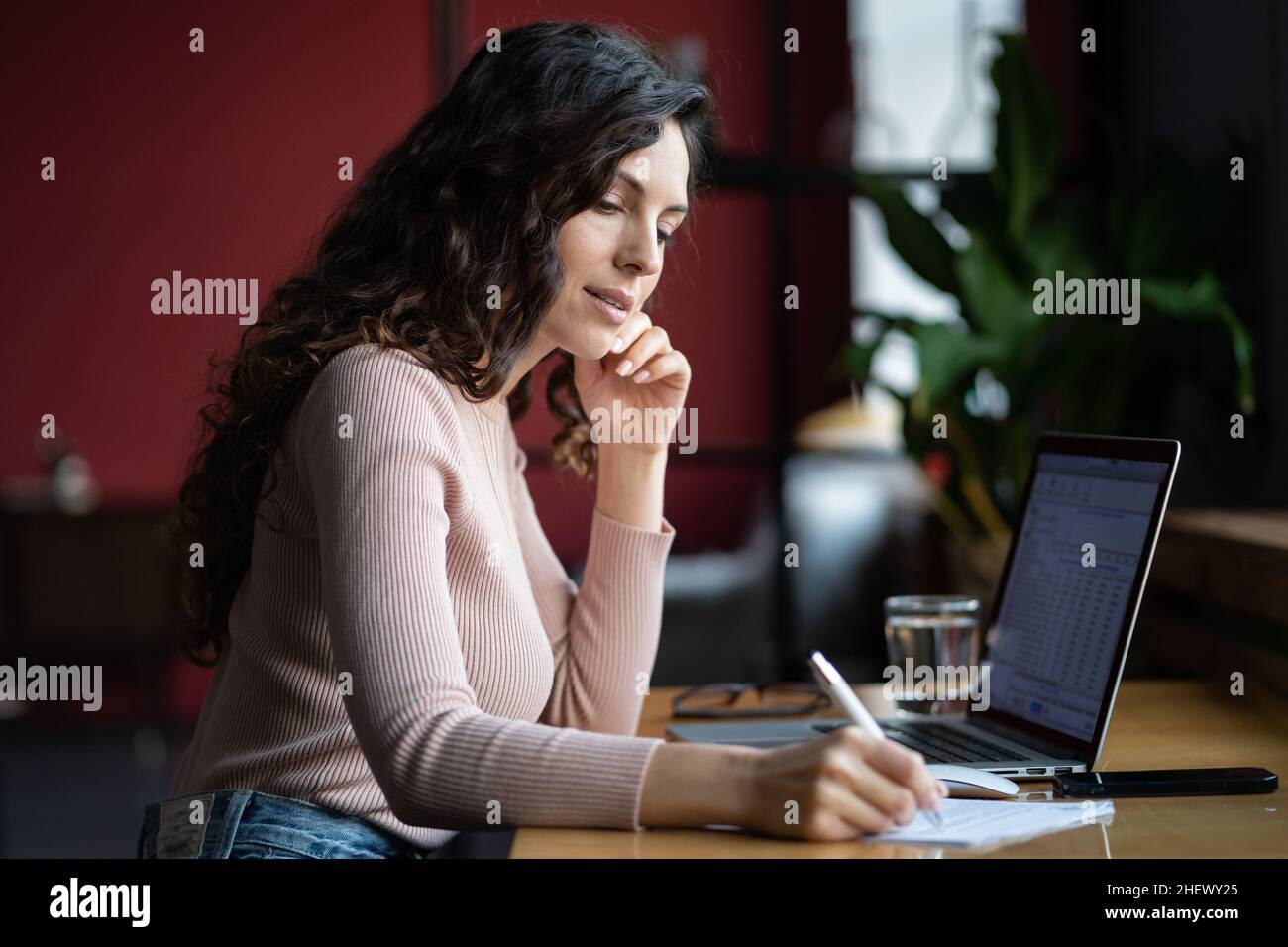 Donna d'affari concentrata che riempie il documento o la forma di imposta, mentre lavora sul computer portatile in ufficio Foto Stock