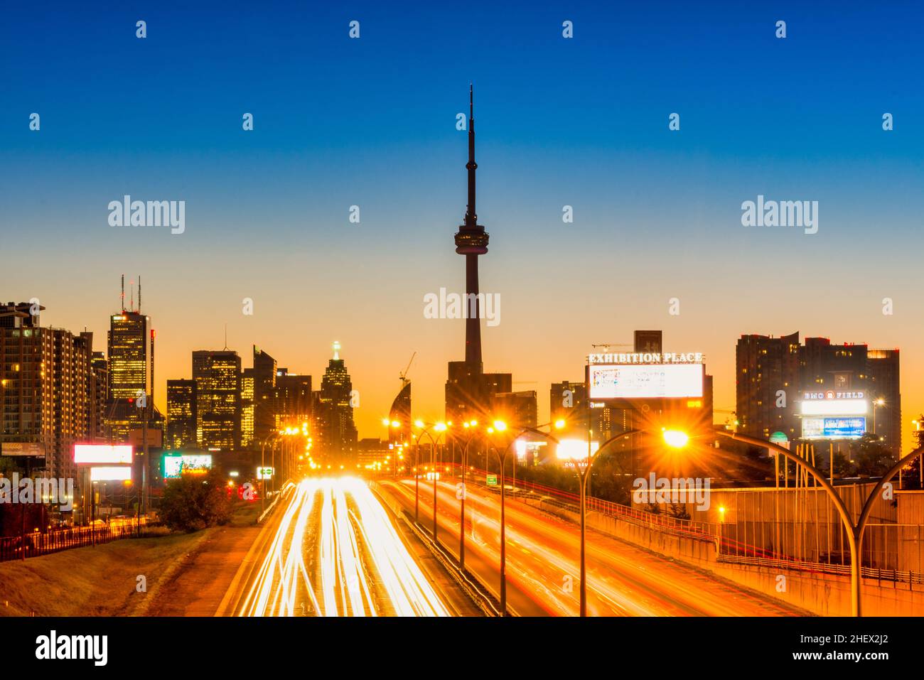 Skyline di Toronto e Gardiner Expressway entrando nel centro di Toronto al tramonto con CN Tower e altri edifici sullo sfondo e traffico a due vie in t Foto Stock