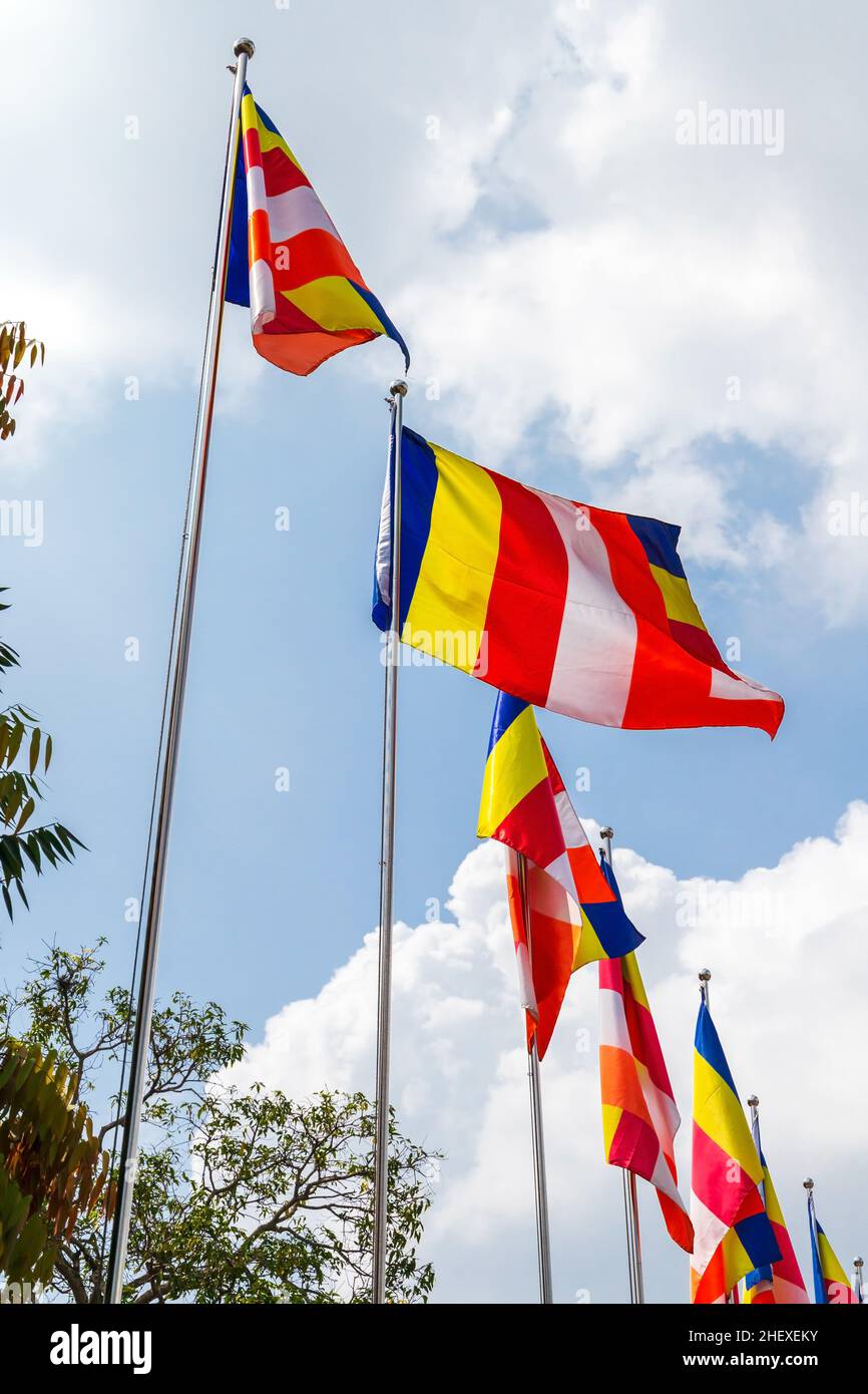 Bandiere buddiste che ondolano in vento sotto il cielo nuvoloso blu all'ingresso di un tempio in Sri Lanka. La bandiera buddista è una bandiera disegnata alla fine del 19th d.c. Foto Stock