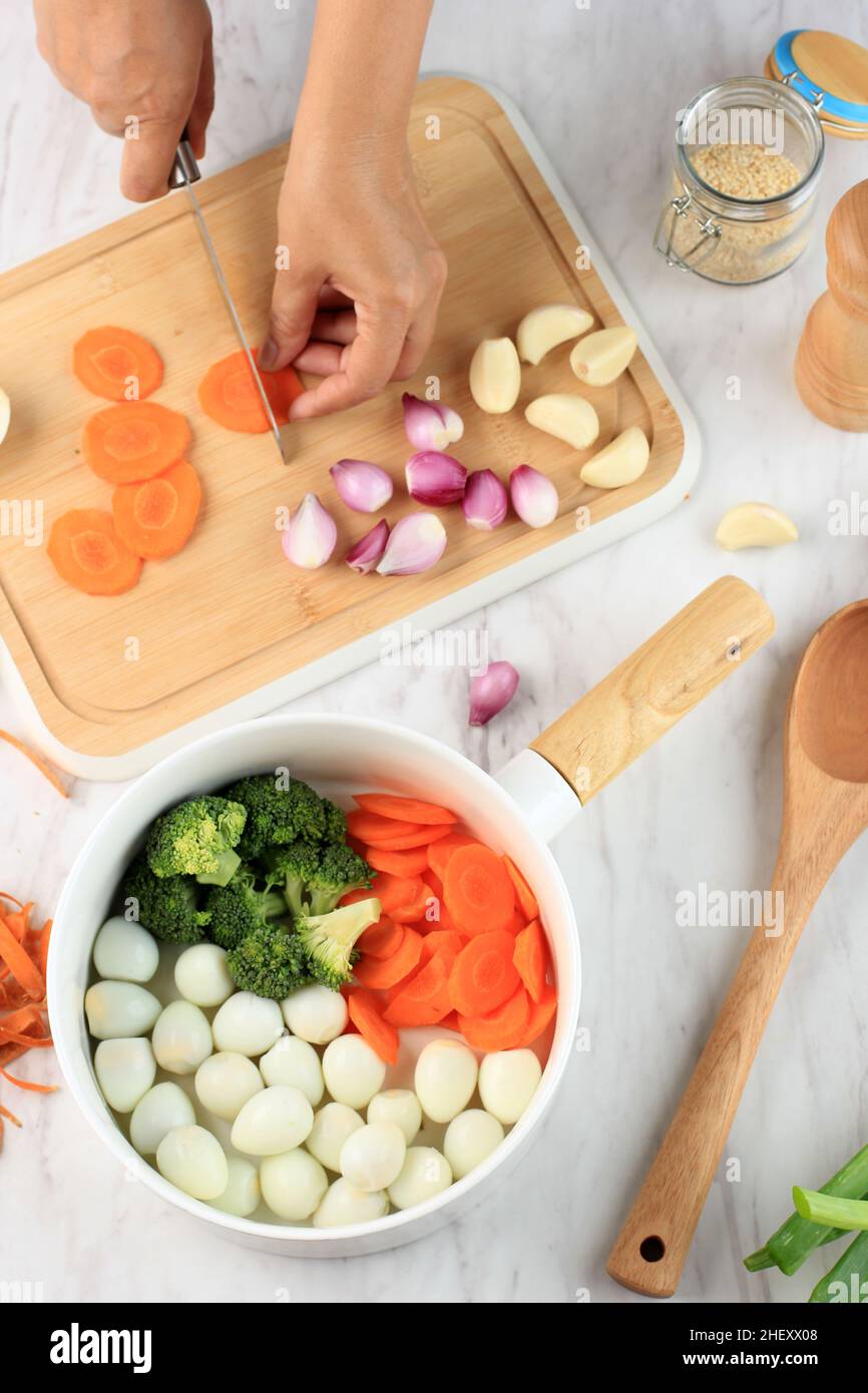 Cucina - le mani dello chef preparano brodo di pollo (brodo o bouillon) con verdure in una pentola. Cucina - grigio cemento piano di lavoro scenario dall'alto (top v Foto Stock