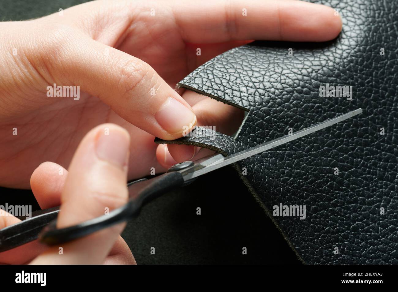Artigiano con forbici taglio fetta di pelle nera macro vista ravvicinata Foto Stock