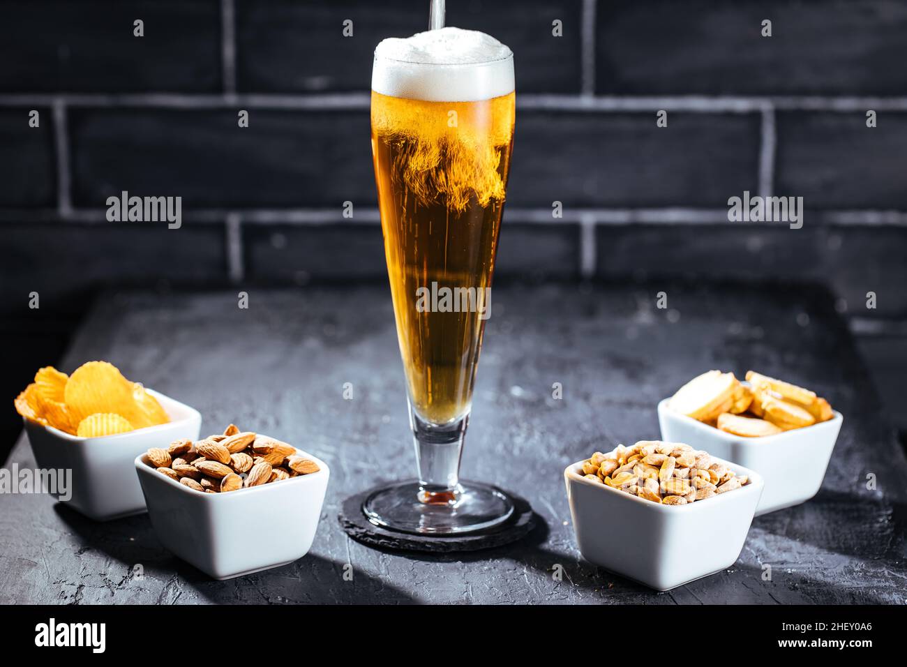 Bicchiere di birra con schiuma e quattro diversi snack Foto Stock