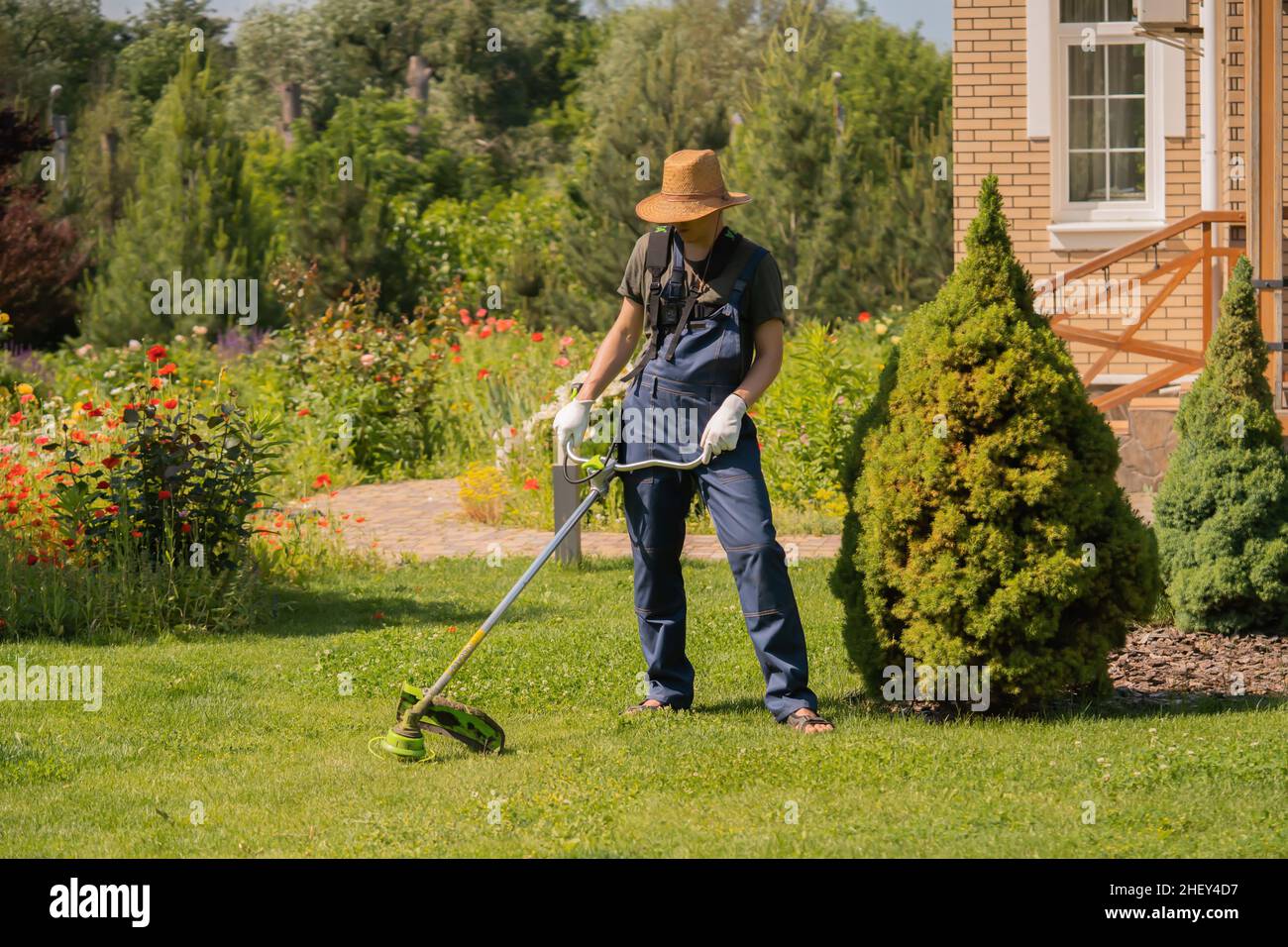 Un giovane uomo con un rasaerba si prende cura dell'erba nel cortile. Foto Stock