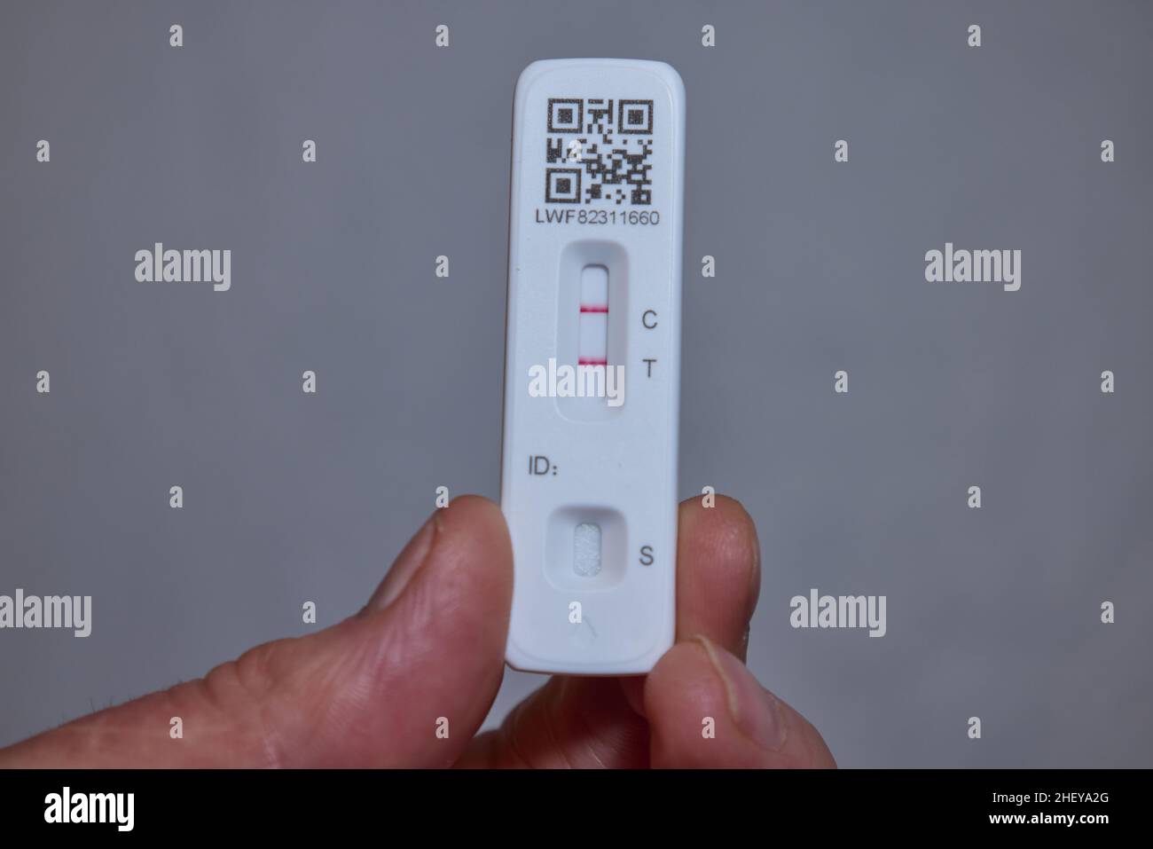 Kit di autotest per antigene a flusso laterale di Coronavirus con tenuta per mano maschio che mostra risultati positivi con fondo grigio liscio Foto Stock