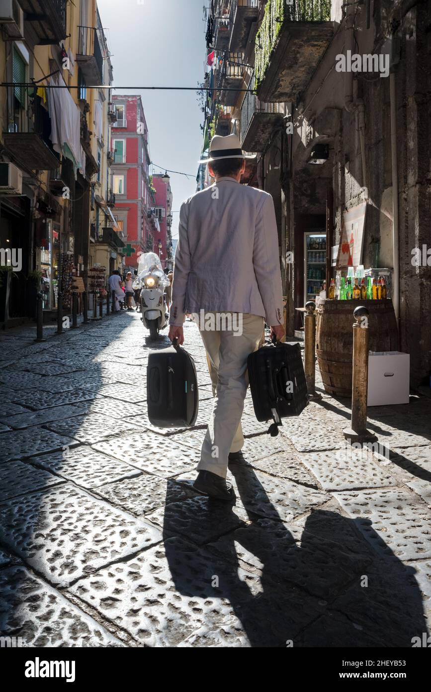Uomo vecchio stile in suite bianca e cappello che porta valigie lungo la vecchia strada di Napoli Foto Stock