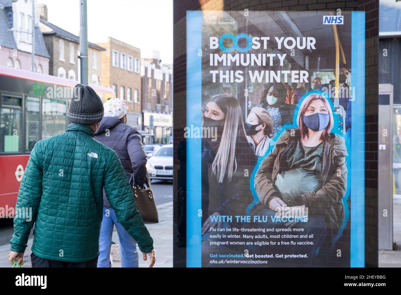 Gli acquirenti passano davanti A un poster alla fermata dell'autobus che consiglia alle persone di aumentare l'immunità in inverno Inghilterra Regno Unito Foto Stock