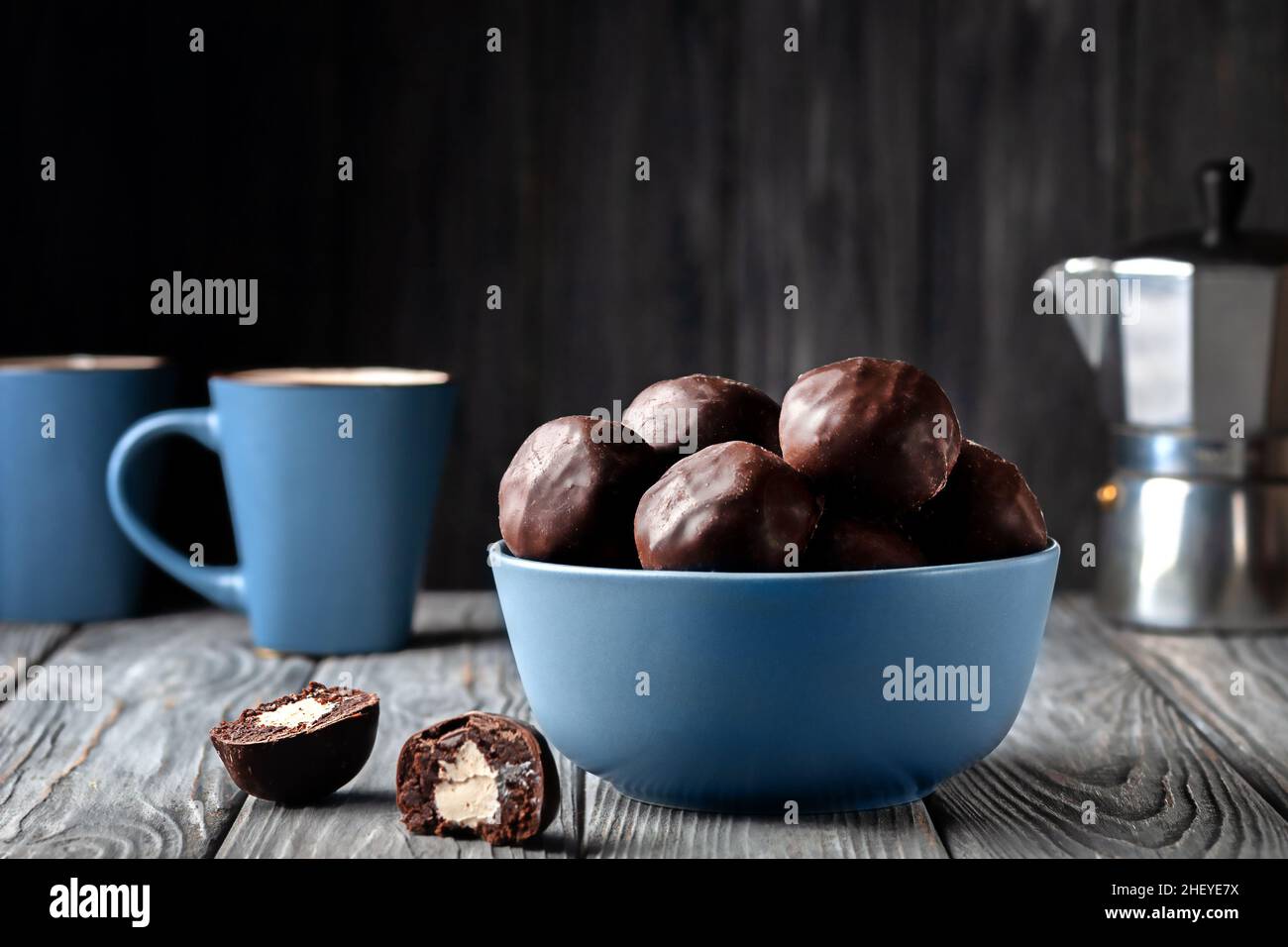 Palline di cioccolato fondente con ripieno di marshmallow e una tazza di caffè su sfondo di legno Foto Stock