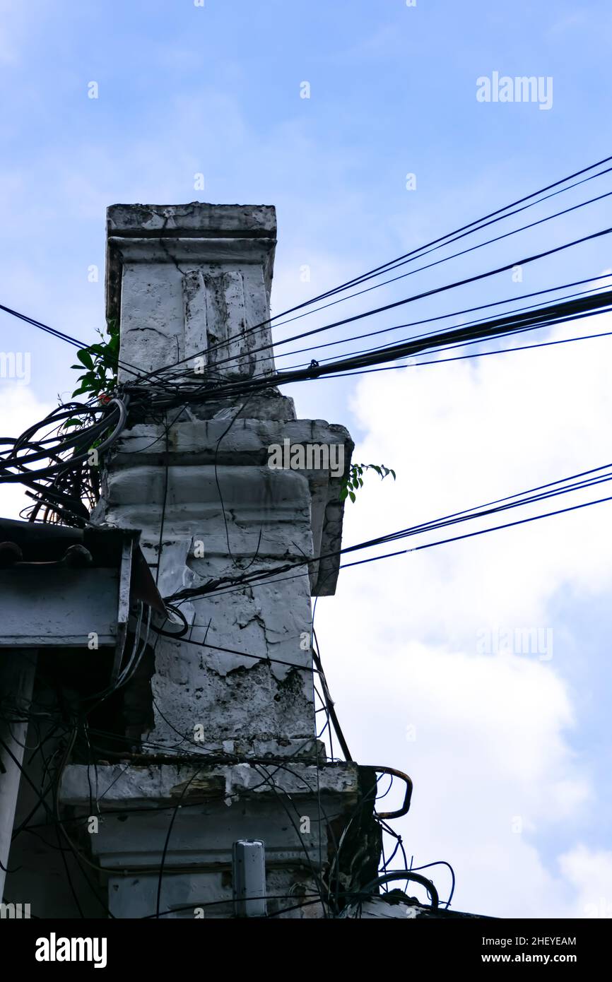 il vecchio pilastro dell'edificio bianco e vintage con cavi elettrici è sospeso sotto il cielo blu chiaro e luminoso Foto Stock