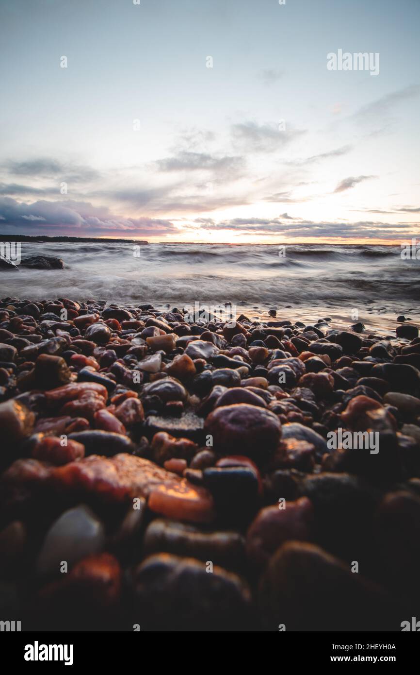 Cielo spettacolare con un mix di rosso, arancio e viola sulle onde del lago Oulujarvi con dettagli sui ciottoli colorati sulla spiaggia di Kajaani, Kainuu Foto Stock