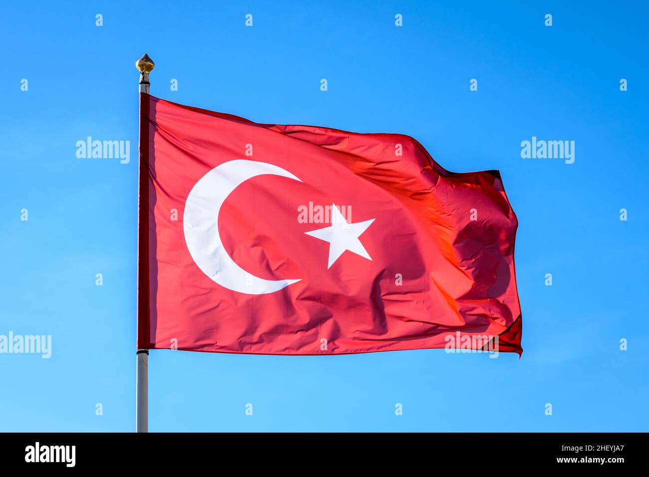 La bandiera nazionale della Turchia vola al vento a pieno palo contro il cielo blu. Foto Stock