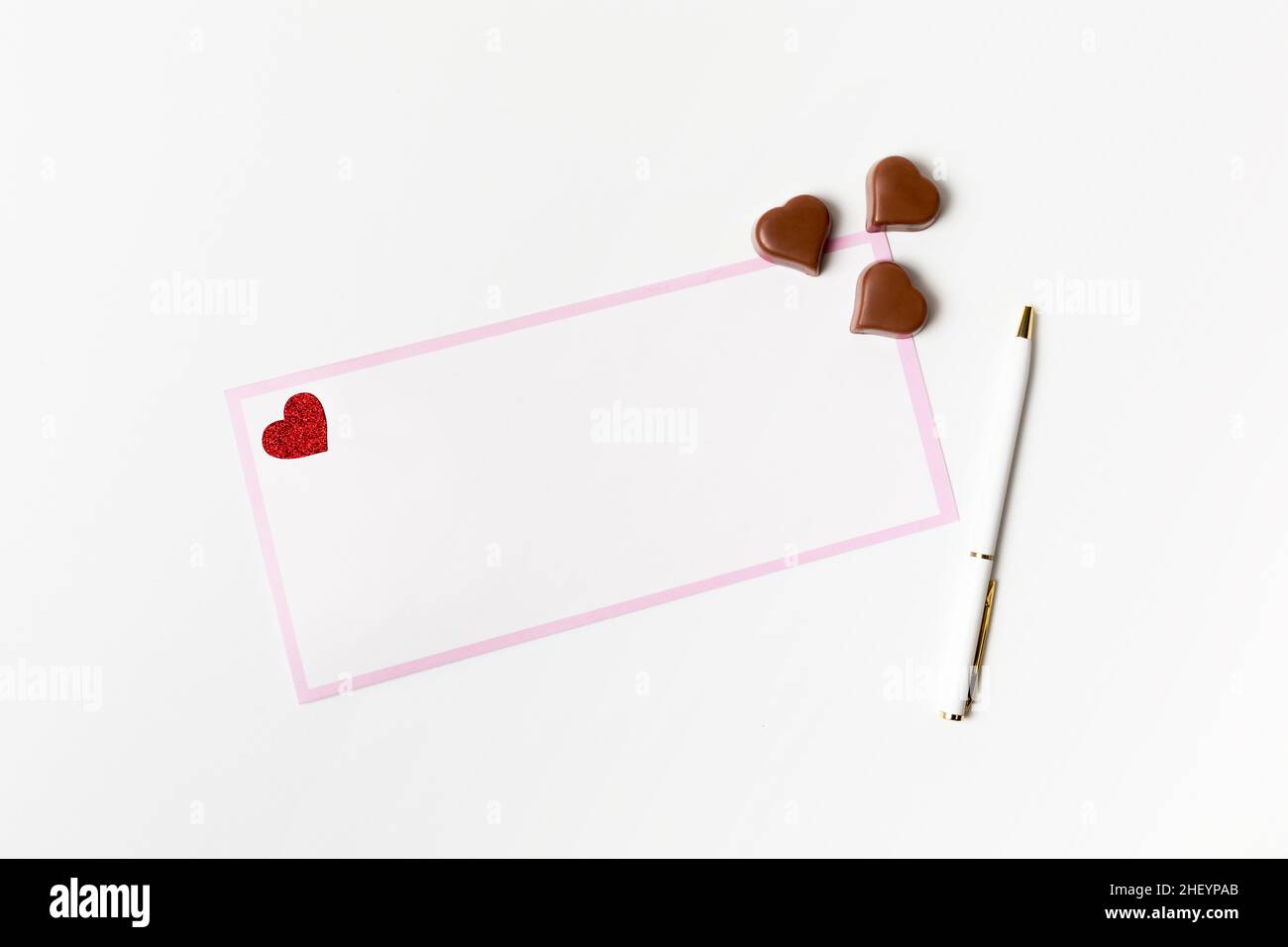 Lettera romantica, biglietto di auguri bianco con penna e caramelle al cioccolato a forma di cuore su sfondo bianco Foto Stock