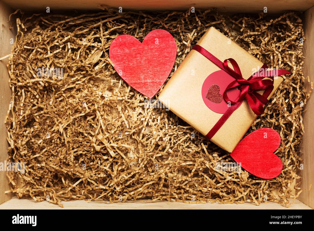 Scatola di legno con presente avvolta in carta artigianale marrone con nastro rosso, riempita con riempitivo di carta, vista dall'alto Foto Stock