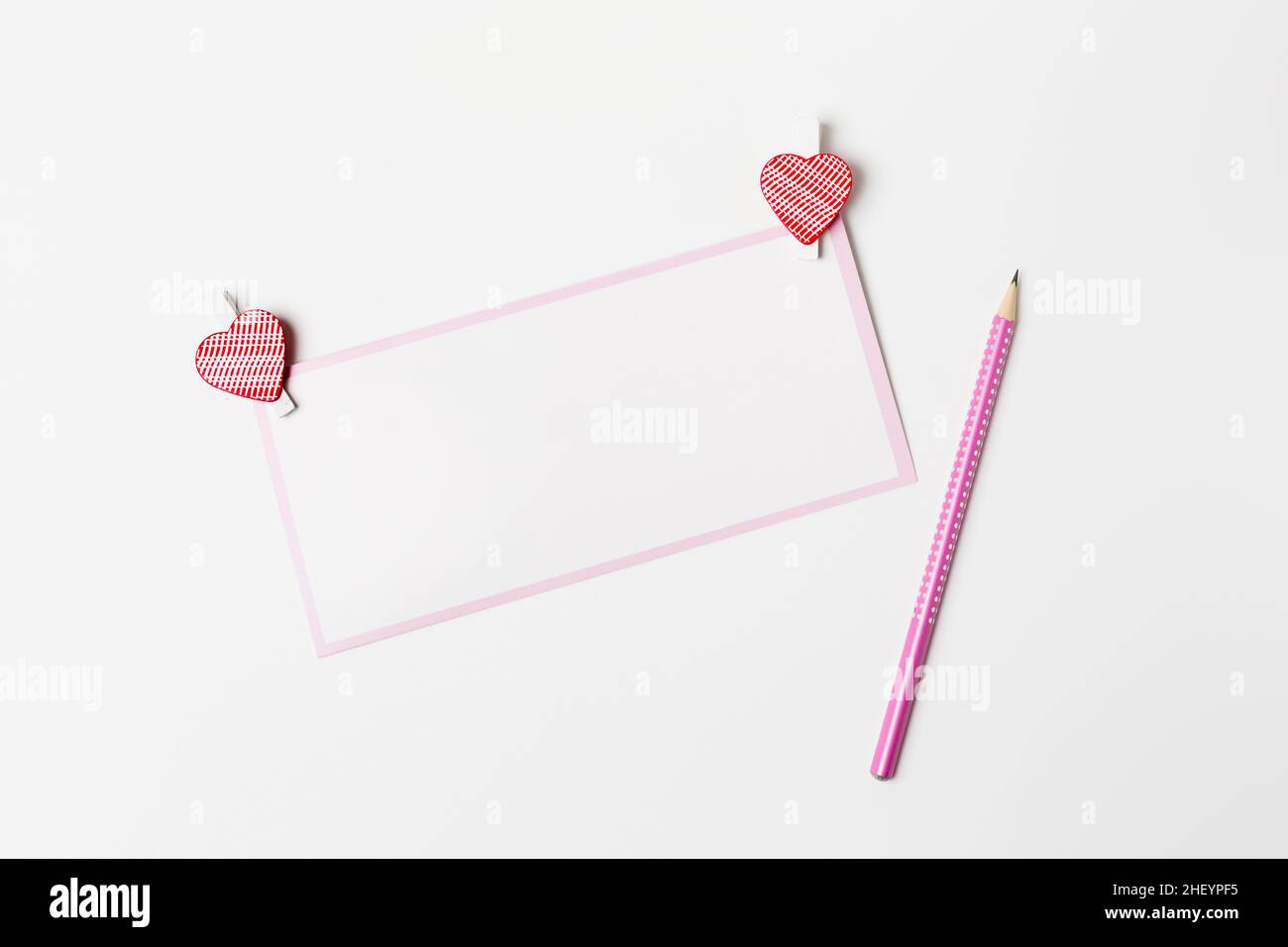 Lettera romantica, biglietto di auguri bianco con una matita rosa e decorazioni a forma di cuore su sfondo bianco, San Valentino congrats Foto Stock
