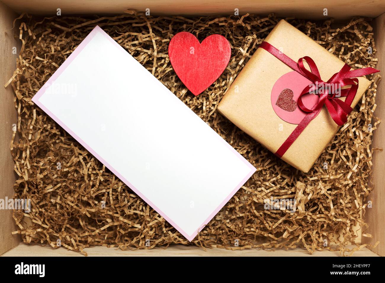 Scatola di legno con presente avvolto in carta artigianale marrone con nastro rosso, con carta vuota vuota, vista dall'alto Foto Stock
