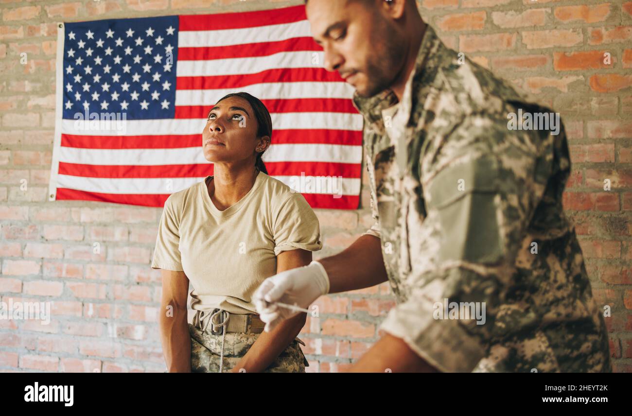 Giovane infermiera maschile che si prepara a vaccinare un servicewoman nell'ospedale dell'esercito. Medica militare americana che si prepara ad amministrare un'iniezione del covid Foto Stock