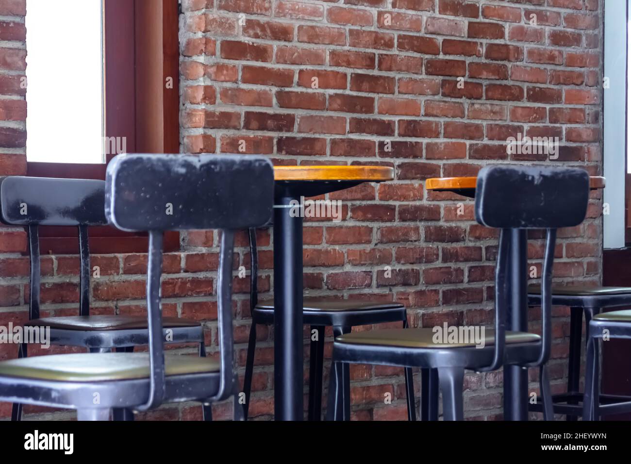 Una linea di sedie industriali nere in metallo si erge oltre un lungo tavolo marrone in legno duro al cafe o al coffee shop interno con pareti in mattoni rossi Foto Stock