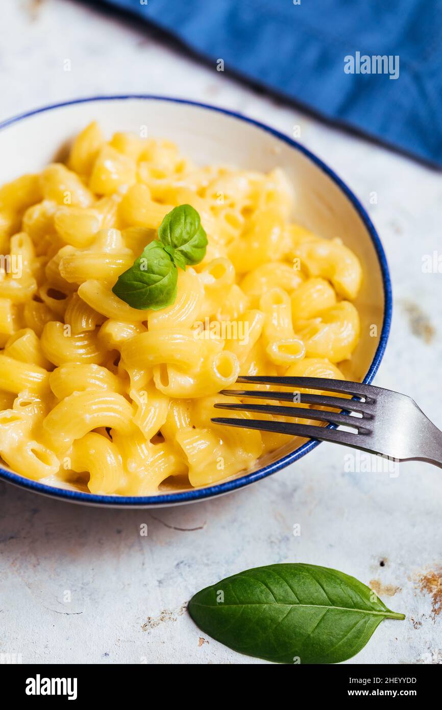 mac classico e formaggio con basilico sulla parte superiore e mac e formaggio cotto in forno sullo sfondo con forchette e macaroni crudi su sfondo rusticžwooden Foto Stock