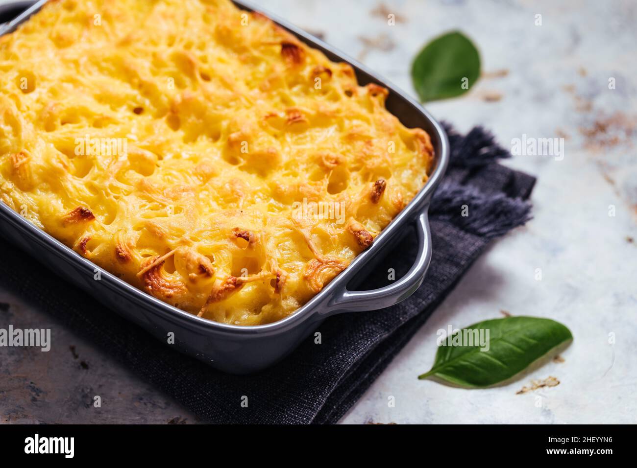 mac classico e formaggio con basilico sulla parte superiore e mac e formaggio cotto in forno sullo sfondo con forchette e macaroni crudi su sfondo rusticžwooden Foto Stock