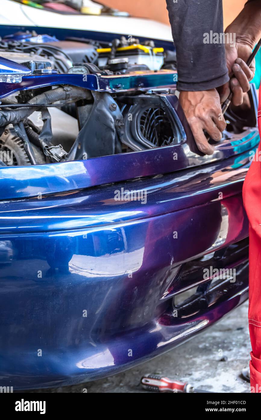 meccanico uomo che fissa e ripara l'automobile blu con le parti non montate al garage auto Foto Stock