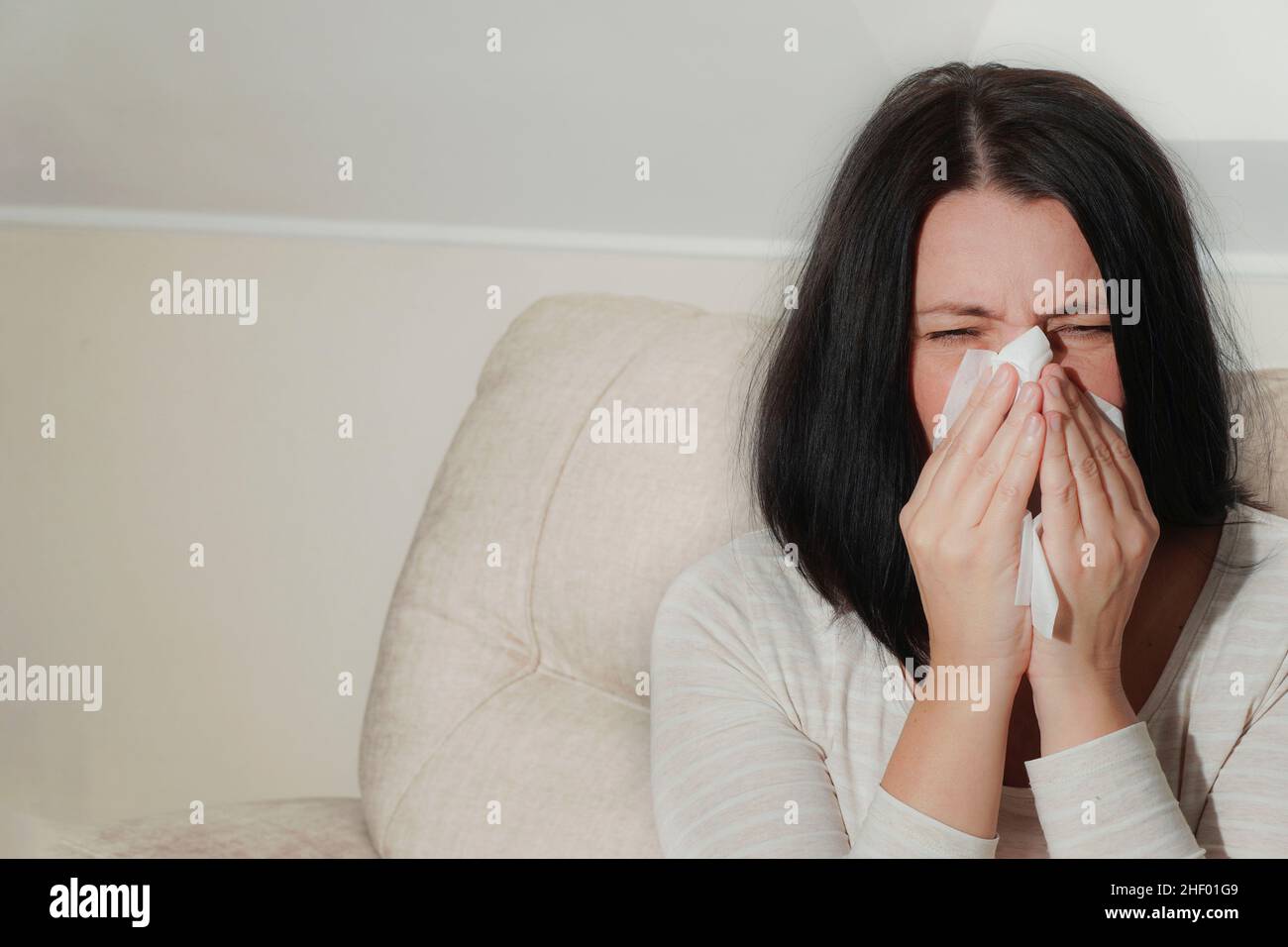 Donna matura di mezza età che soffre di rinite allergica a casa. Sintomi di raffreddore o allergia. La donna starnutisce in tessuto bianco. Foto Stock