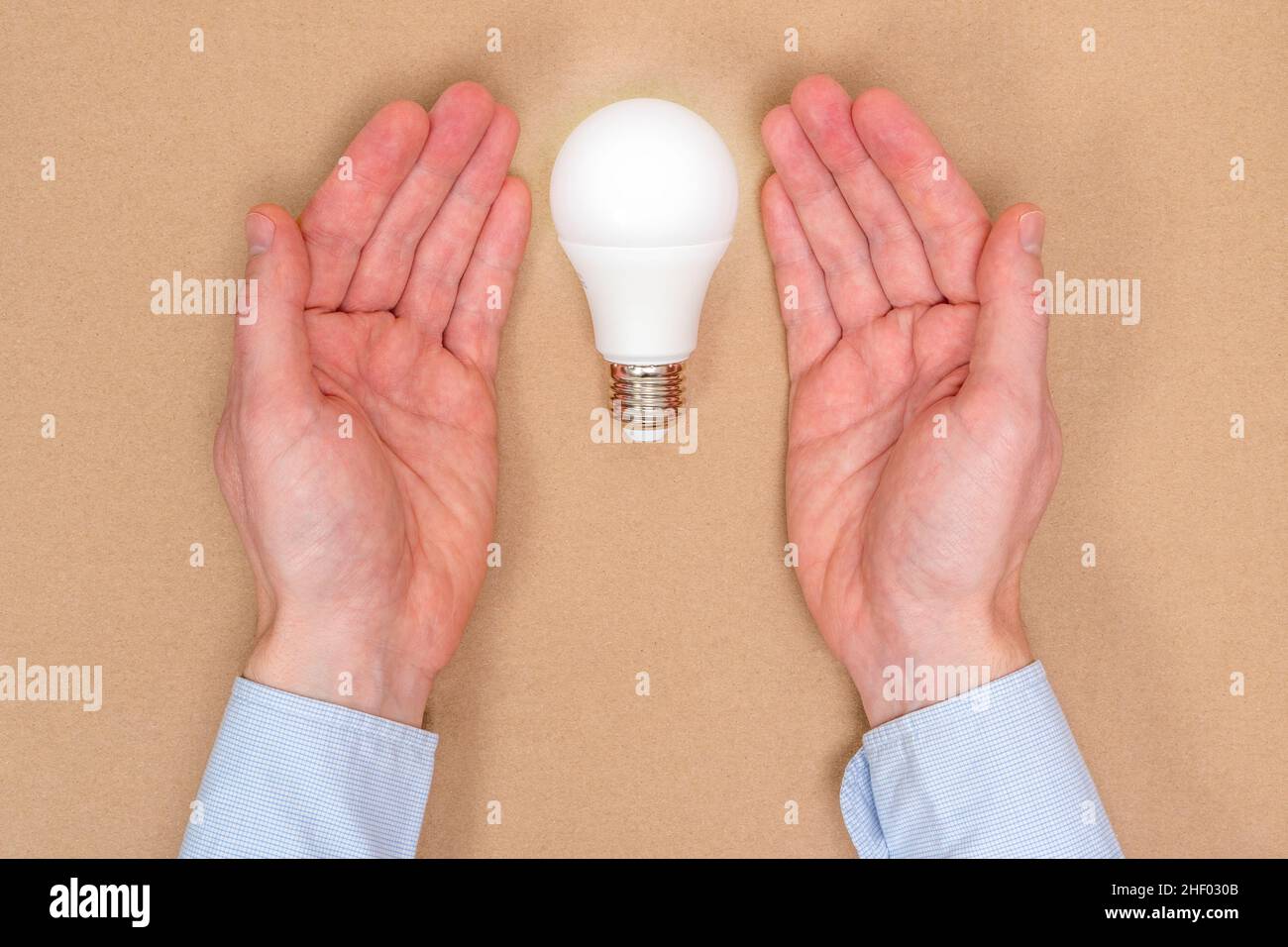 Un'immagine concettuale di una nuova idea, di una nuova nascita. La lampadina a LED è coperta dalle mani. Foto Stock