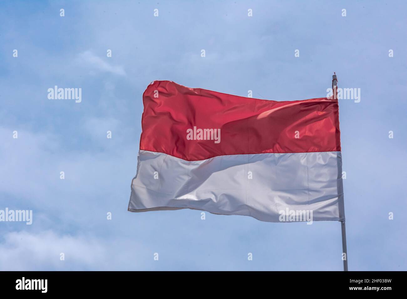Bandiera nazionale indonesiana bianca e rossa che sale e sotto il cielo azzurro chiaro e luminoso Foto Stock