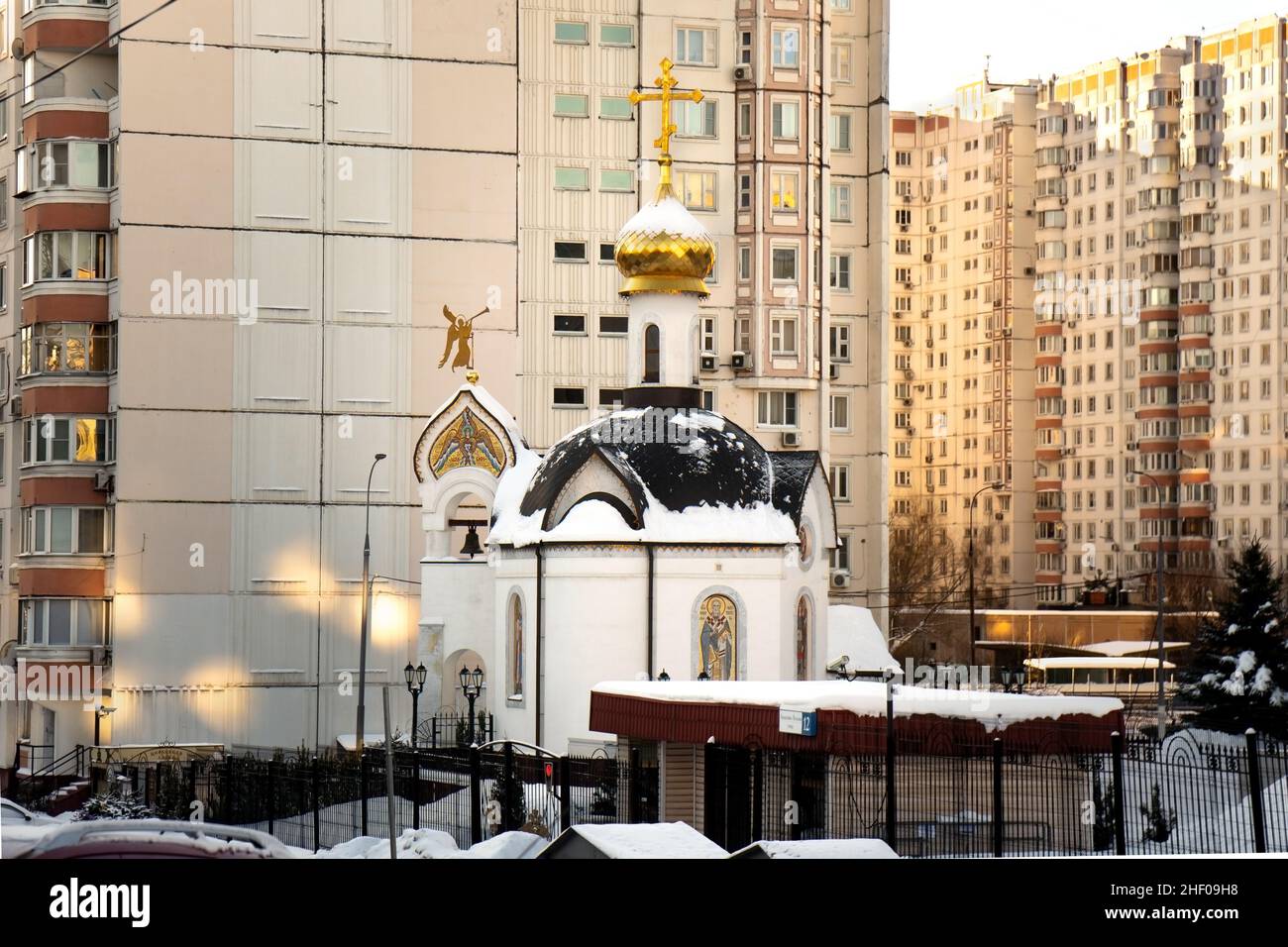 Mosca, Russia-7 gennaio 2022. Piccola chiesa della città situata tra le grandi case residenziali a Mosca in freddo giorno di sole inverno Foto Stock