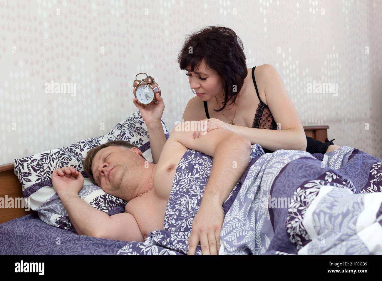 Una donna si sveglia con un uomo che dormiva e che aveva dormito per lavorare mostrando una sveglia. Foto Stock