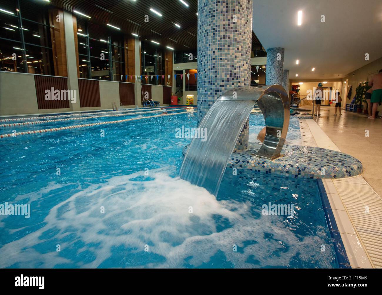 una parte bassa della piscina con una cascata di massaggio. Persone in lontananza. Le persone nuotano in acqua - non sono molto visibili Foto Stock