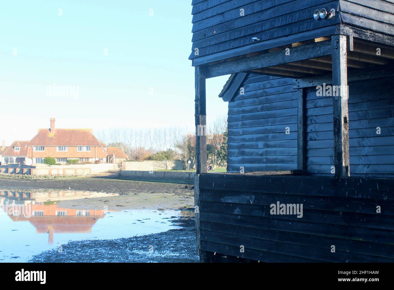Il Raptackle, nero tempo-imbarcato vecchio magazzino su Bosham Quay con residenza in background. Riflessi. Foto Stock