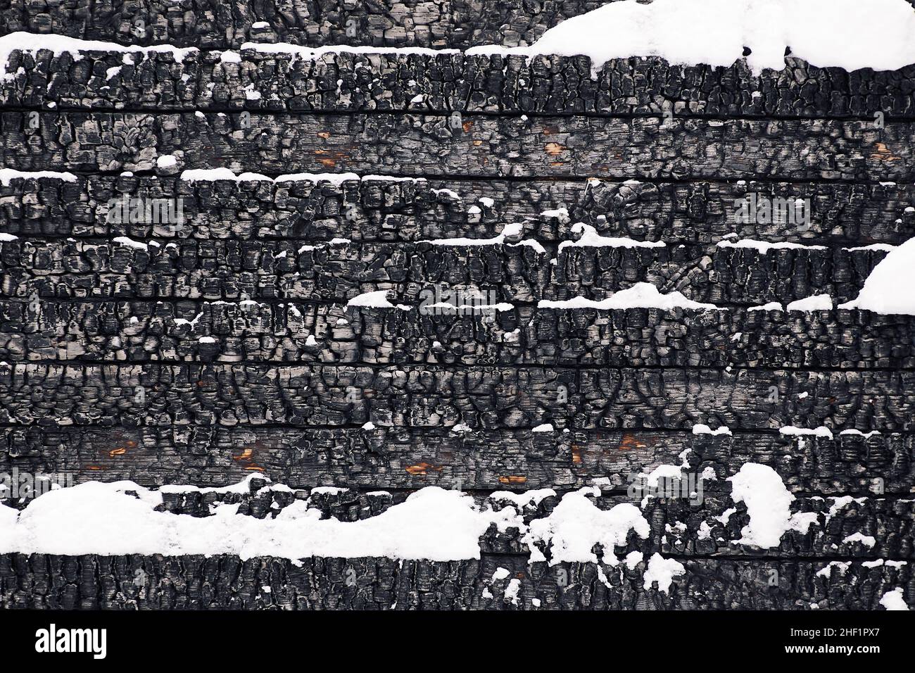 Parte del muro di legno di una casa bruciata coperta di neve. Struttura di legno bruciato Foto Stock