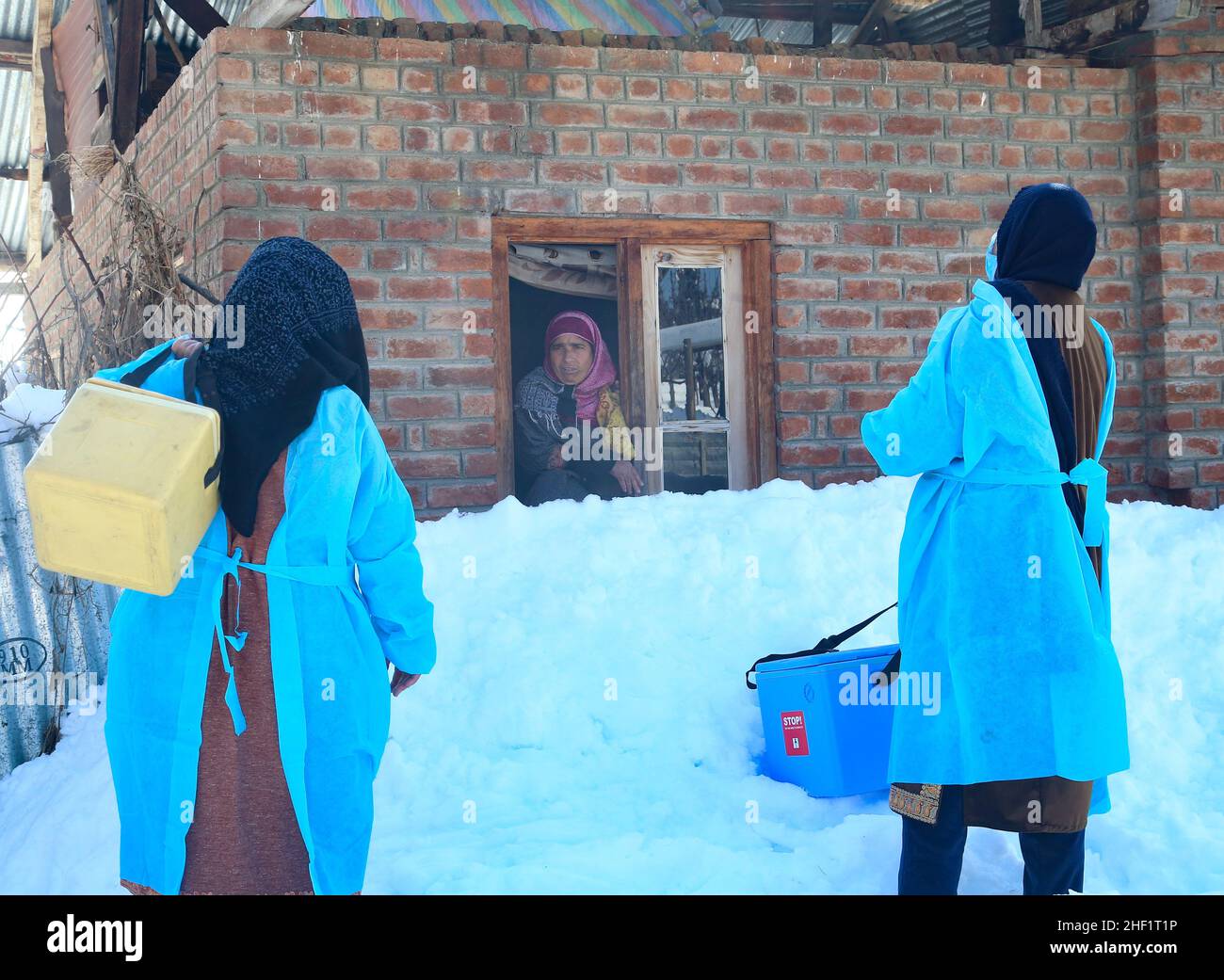 Gli operatori sanitari parlano con la donna del Kashmiri mentre arrivano durante una campagna di vaccinazione porta a porta al villaggio di Malvaa Snowbound nel distretto di Baramulla nel Kashmir settentrionale, a circa 56 chilometri da Srinagar, la capitale estiva del Kashmir indiano. Nonostante le strade fredde e completamente innevate, questi operatori sanitari nella valle del Kashmir stanno sfidando le condizioni meteorologiche difficili e andando da porta a porta per vaccinare people.in un'area lontana-flung della valle del Kashmir, un team di operatori medici che trasportano scatole di vaccinazione e altri materiali inizia la loro campagna di vaccinazione mentre camminano sulla nar coperta di neve Foto Stock