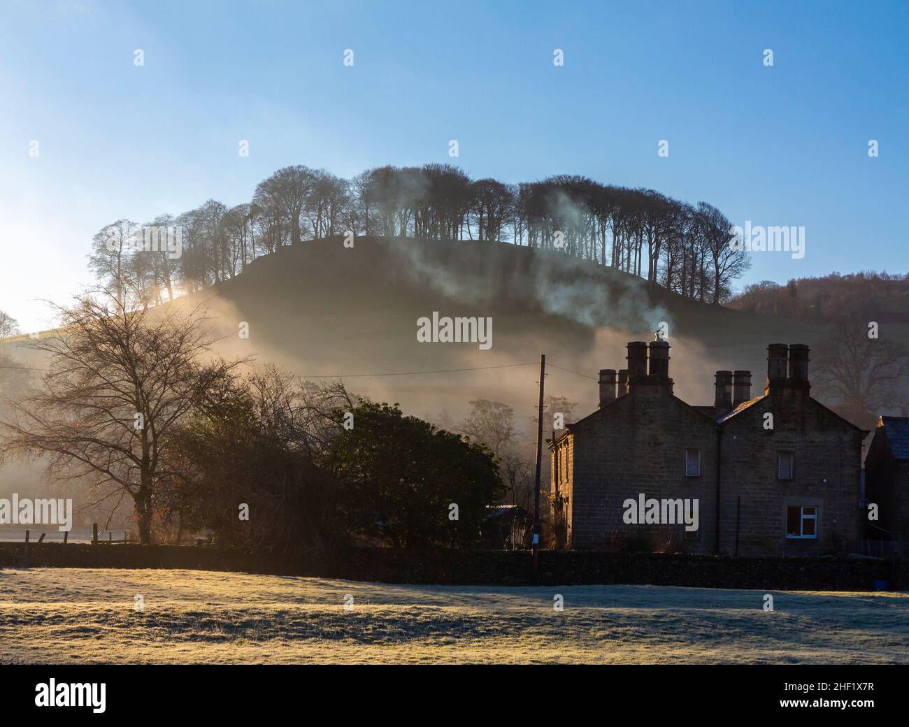 Gelo paesaggio coperto con case e alberi a Rowsley nel Derbyshire Peak District Inghilterra UK con Peak Tor o Pillow Hill in lontananza. Foto Stock