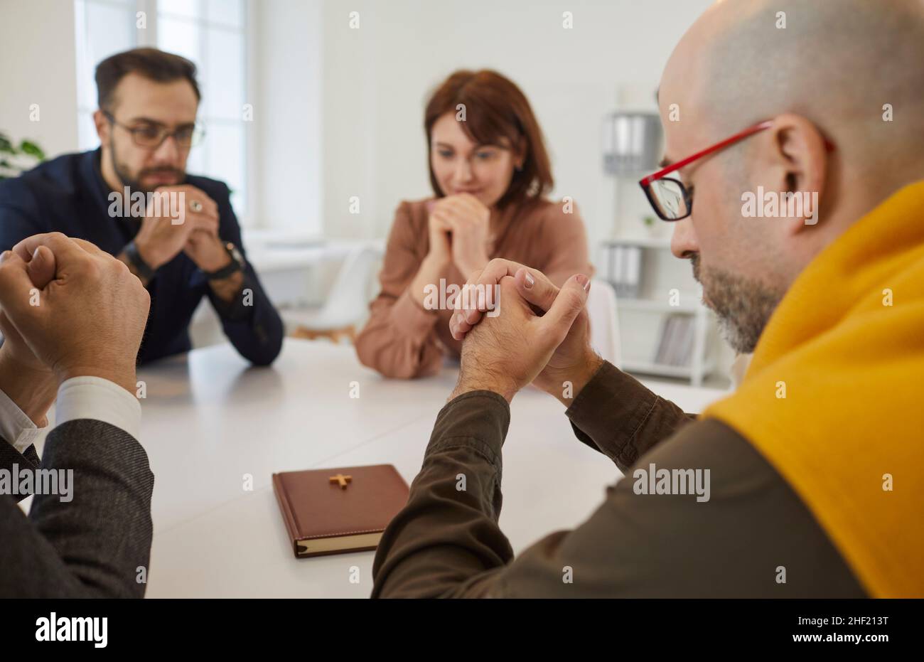 Gruppo di persone che pregano Dio seduti attorno al tavolo con la Sacra Bibbia Foto Stock