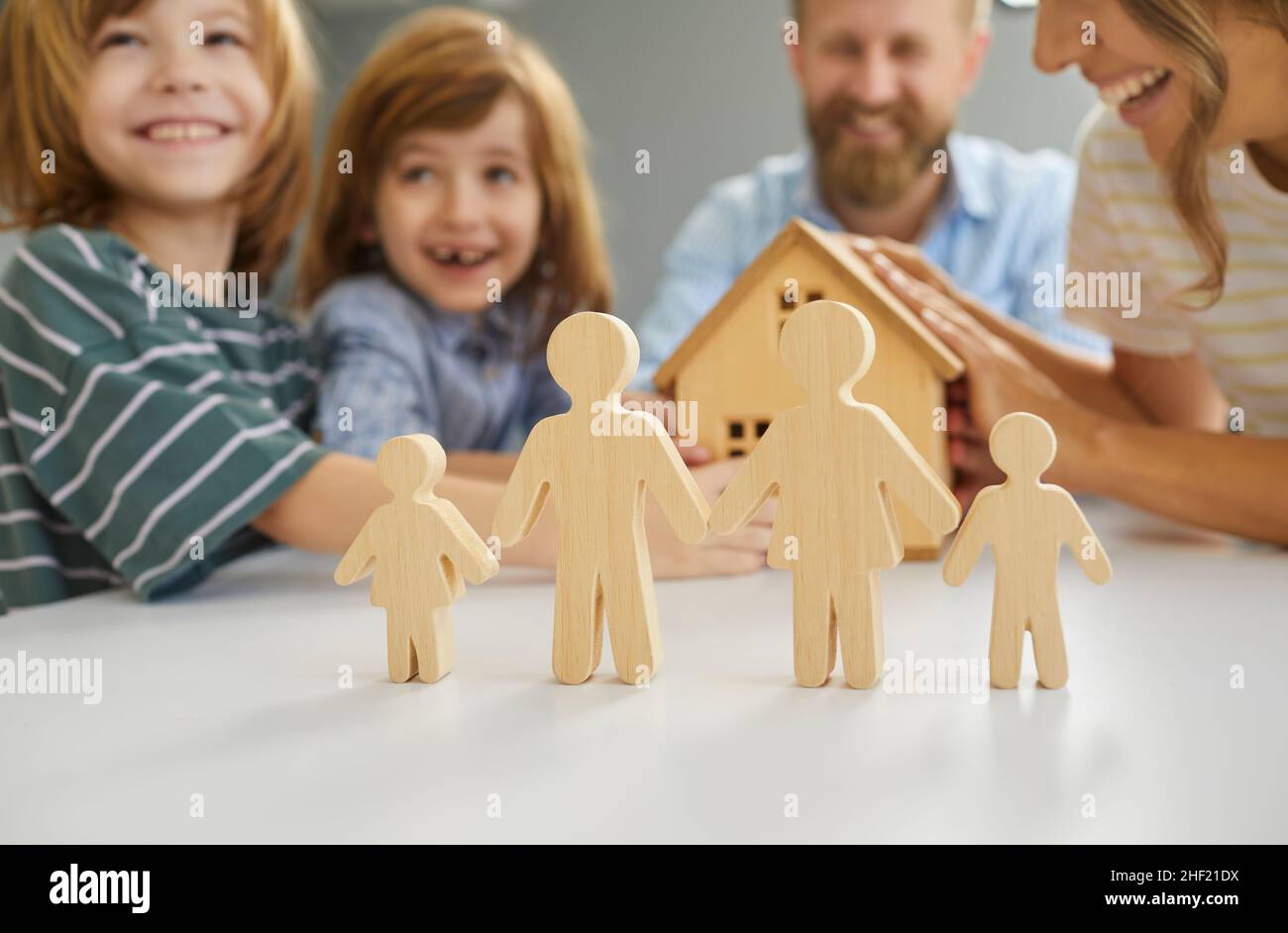 Piccole figure di mamma, papà e bambini in primo piano, e famiglia felice con casa giocattolo in background Foto Stock