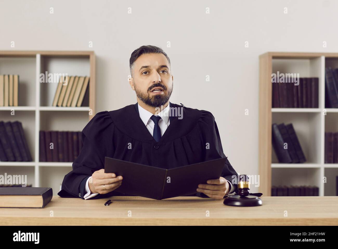 Giovane giudice in abito seduto al suo tavolo in aula e leggere la sentenza Foto Stock